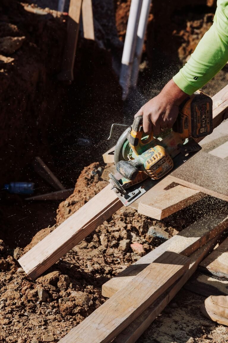A construction worker uses a circular saw to cut timber on a sunny outdoor site.
