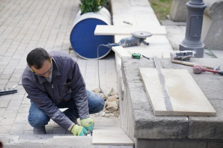 A focused mason wearing protective gear, laying stone tiles outdoors, showcasing craftsmanship.